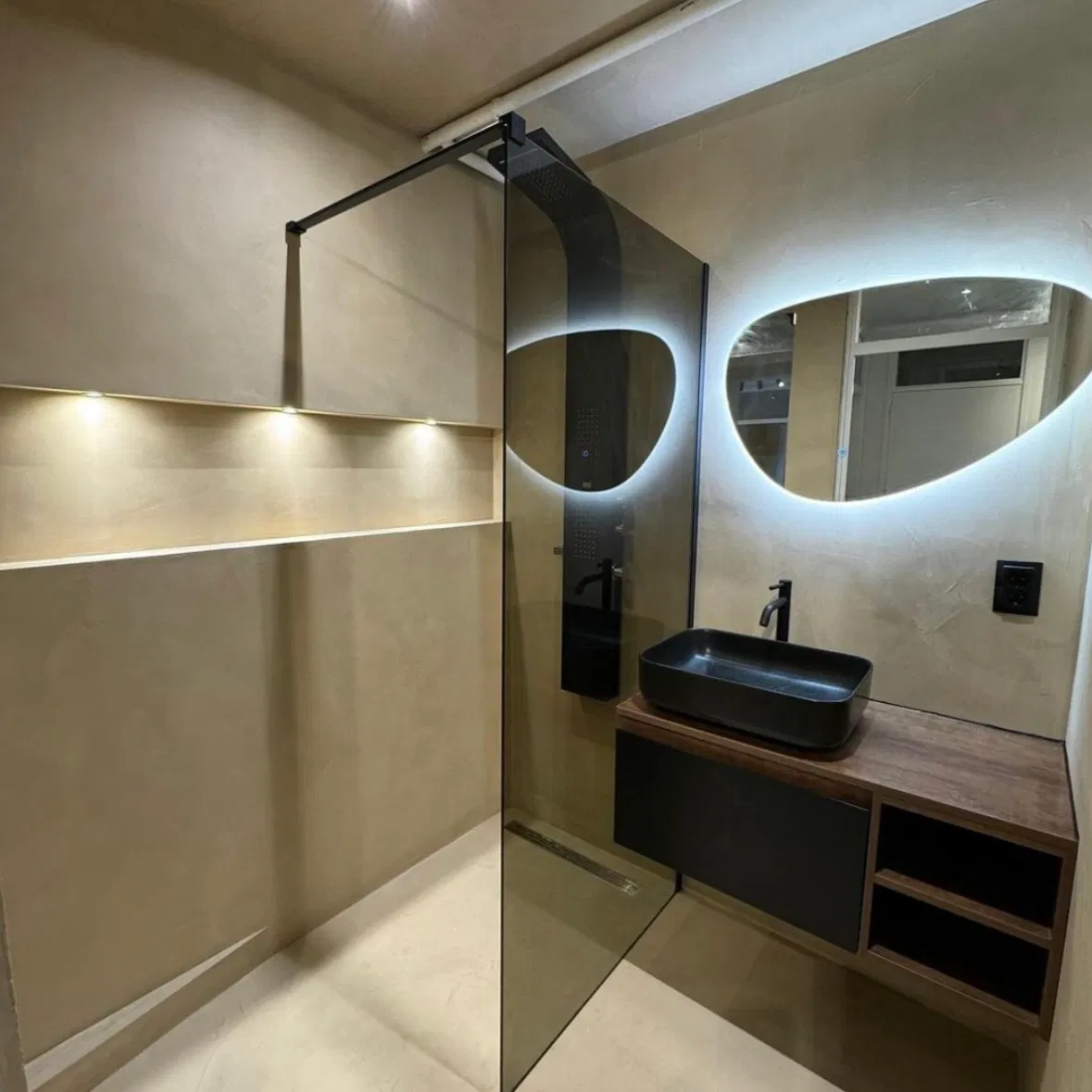 Modern bathroom with a glass shower partition, circular backlit mirror, and a black vessel sink on a wood vanity.