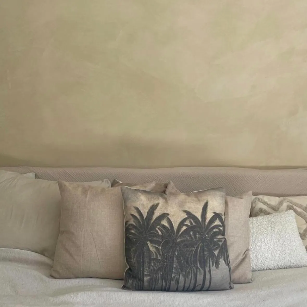 Beige couch with several neutral throw pillows, including a palm tree print pillow in front.